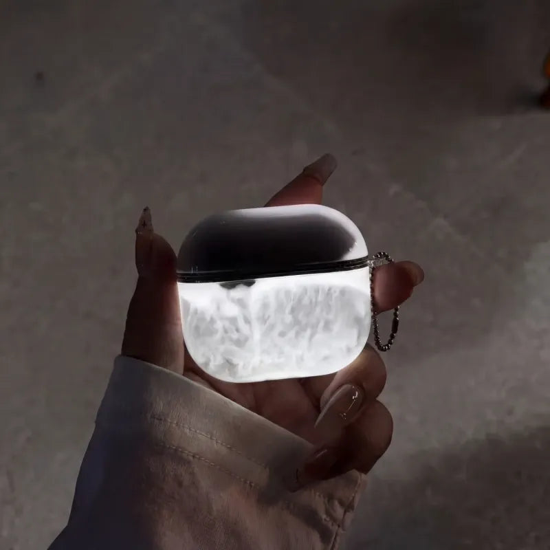 Hand holding a midnight smoke coloured glow in the dark moveable sand airpod case