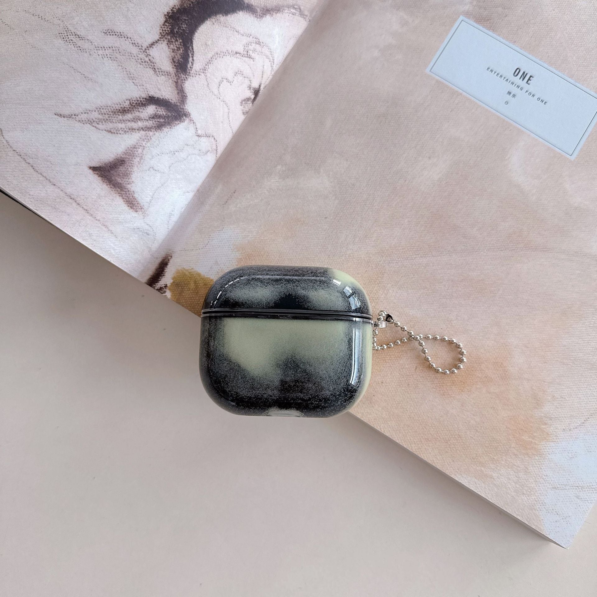 Midnight smoke air pod case with a keychain on a textured surface
